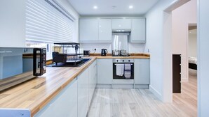 A modern kitchen with white cabinets, a wooden countertop, a built-in oven, and a window with blinds. - Sleek & Exquisite 3 Bedroom Home (Colchester)