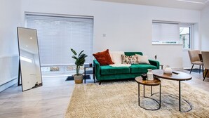 A modern living room with a green sofa, a round coffee table, and a large mirror. - Sleek & Exquisite 3 Bedroom Home (Colchester)