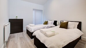 A bedroom with two beds, a dresser, a radiator, and a window with blinds. - Sleek & Exquisite 3 Bedroom Home (Colchester)