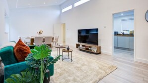 A modern living room with a flat-screen TV, a teal sofa, and a dining area with a table and chairs. - Sleek & Exquisite 3 Bedroom Home (Colchester)