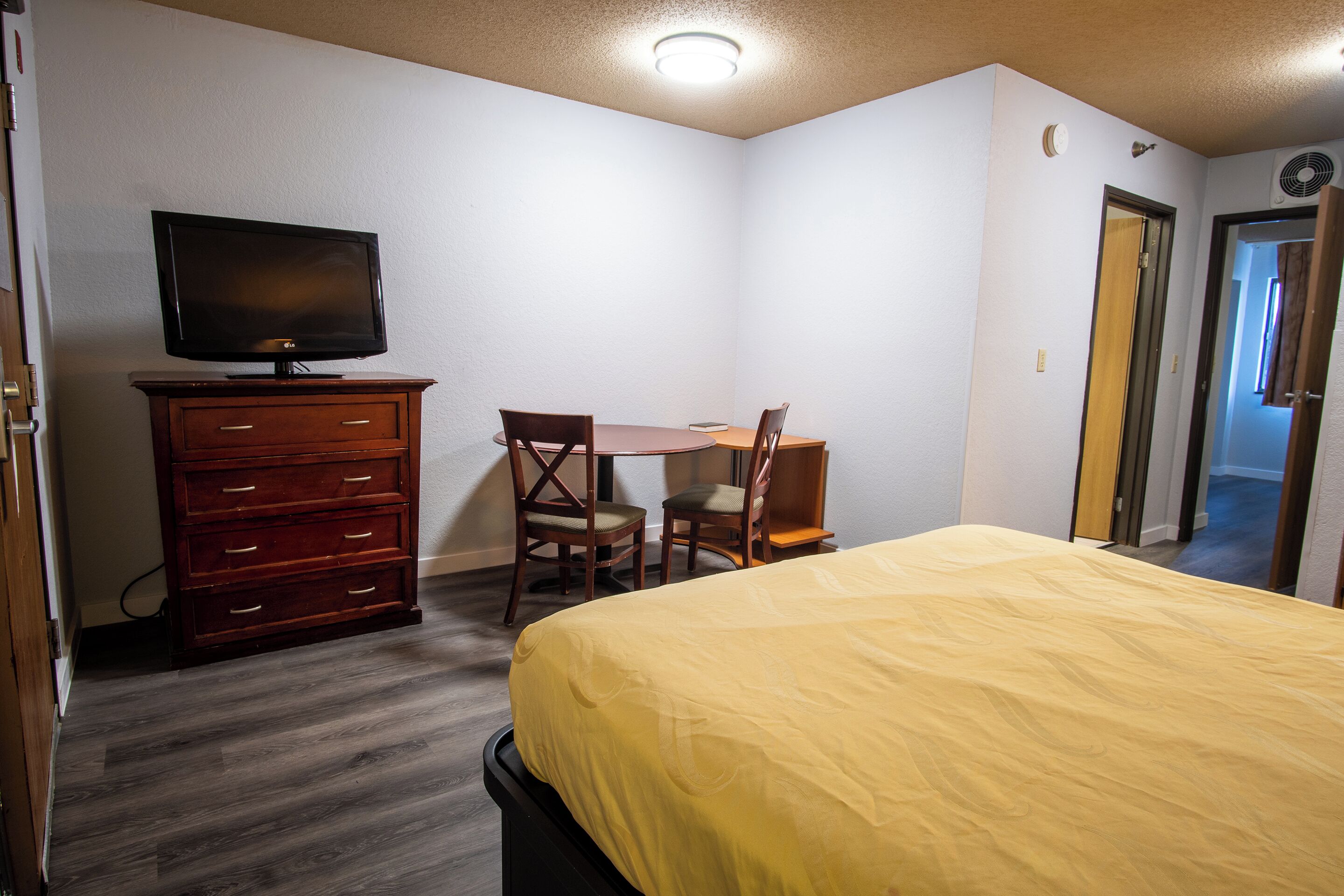 Un dormitorio con cama, cómoda, televisor y escritorio con dos sillas.