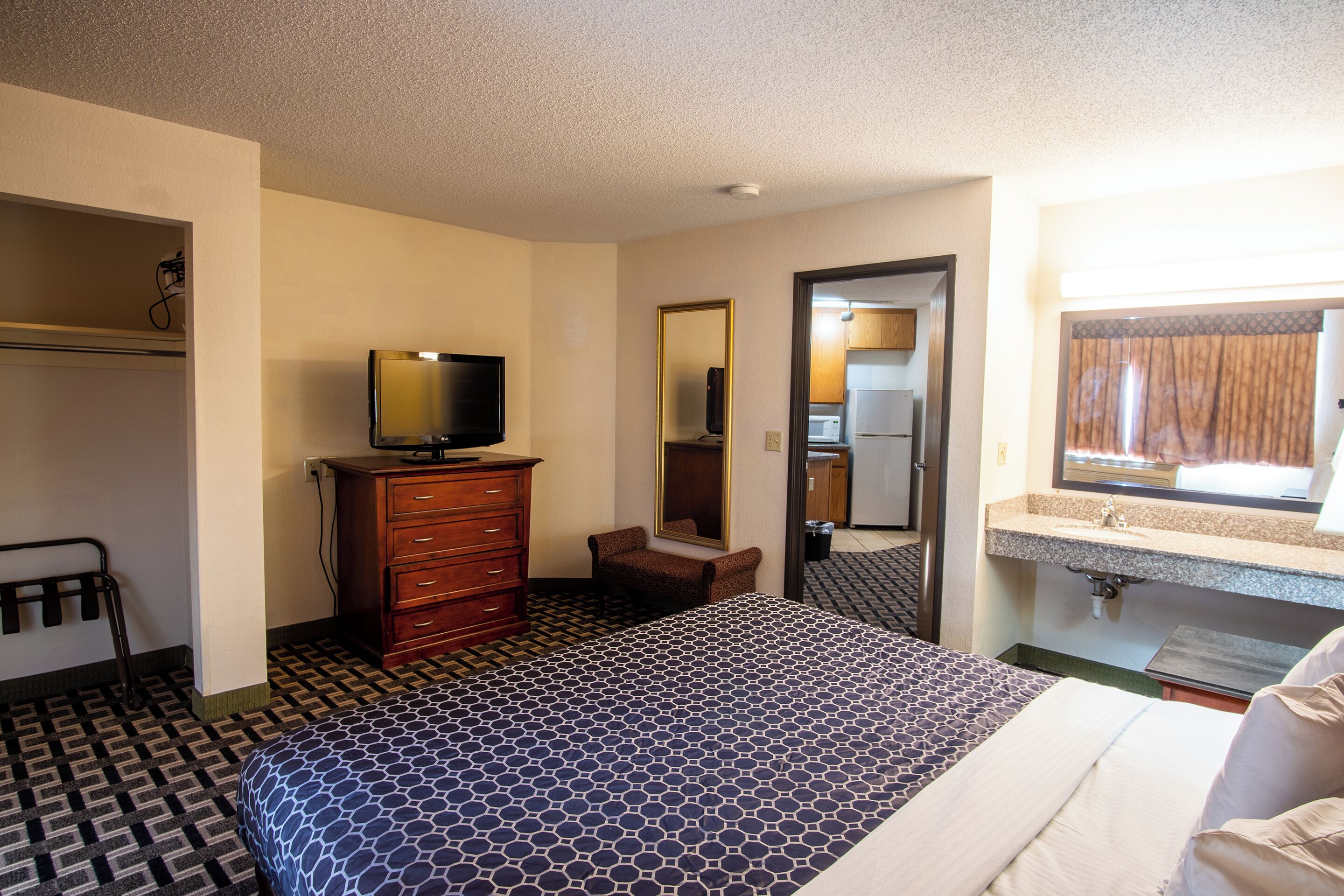 Una habitación de hotel con cama, cómoda, televisor, espejo y baño.