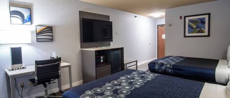 A hotel room with a bed, desk, chair, TV, and artwork on the walls.