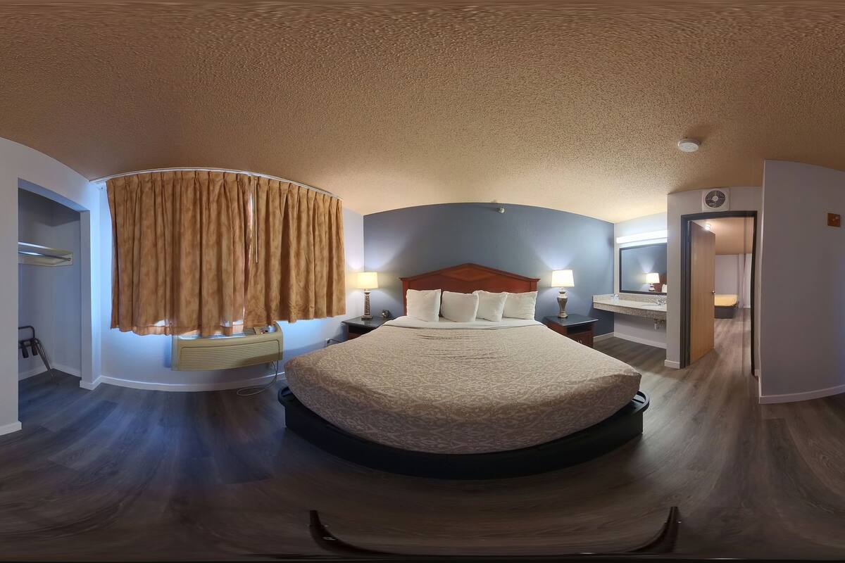 A hotel room with a large bed, a TV, a dresser, and a bathroom with a mirror and sink.