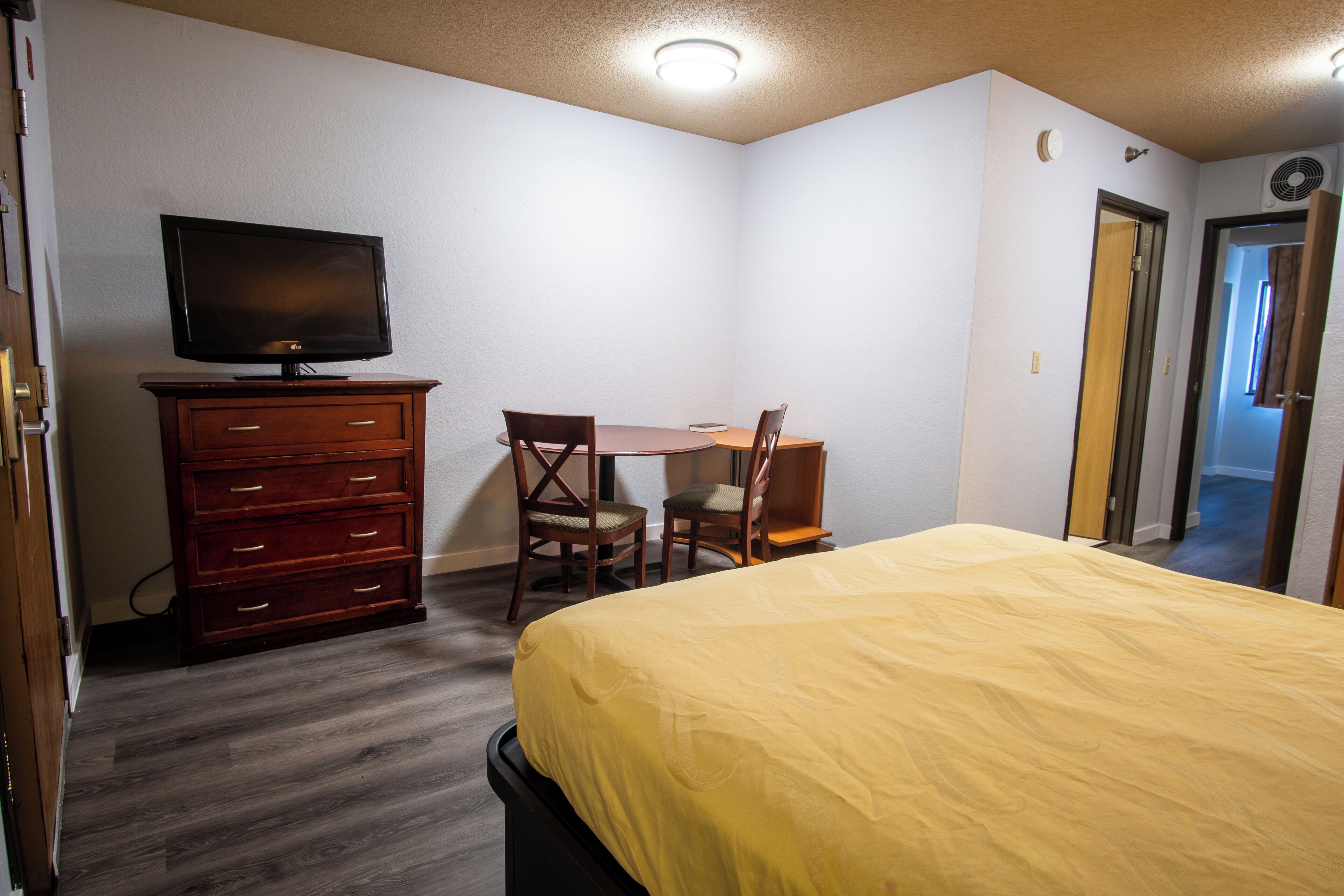A bedroom with a bed, a dresser, a television, and a desk with two chairs.