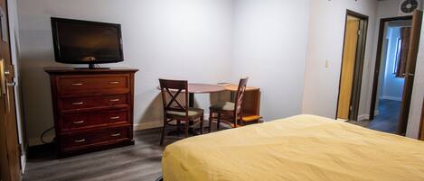 A bedroom with a bed, a dresser, a television, and a desk with two chairs.