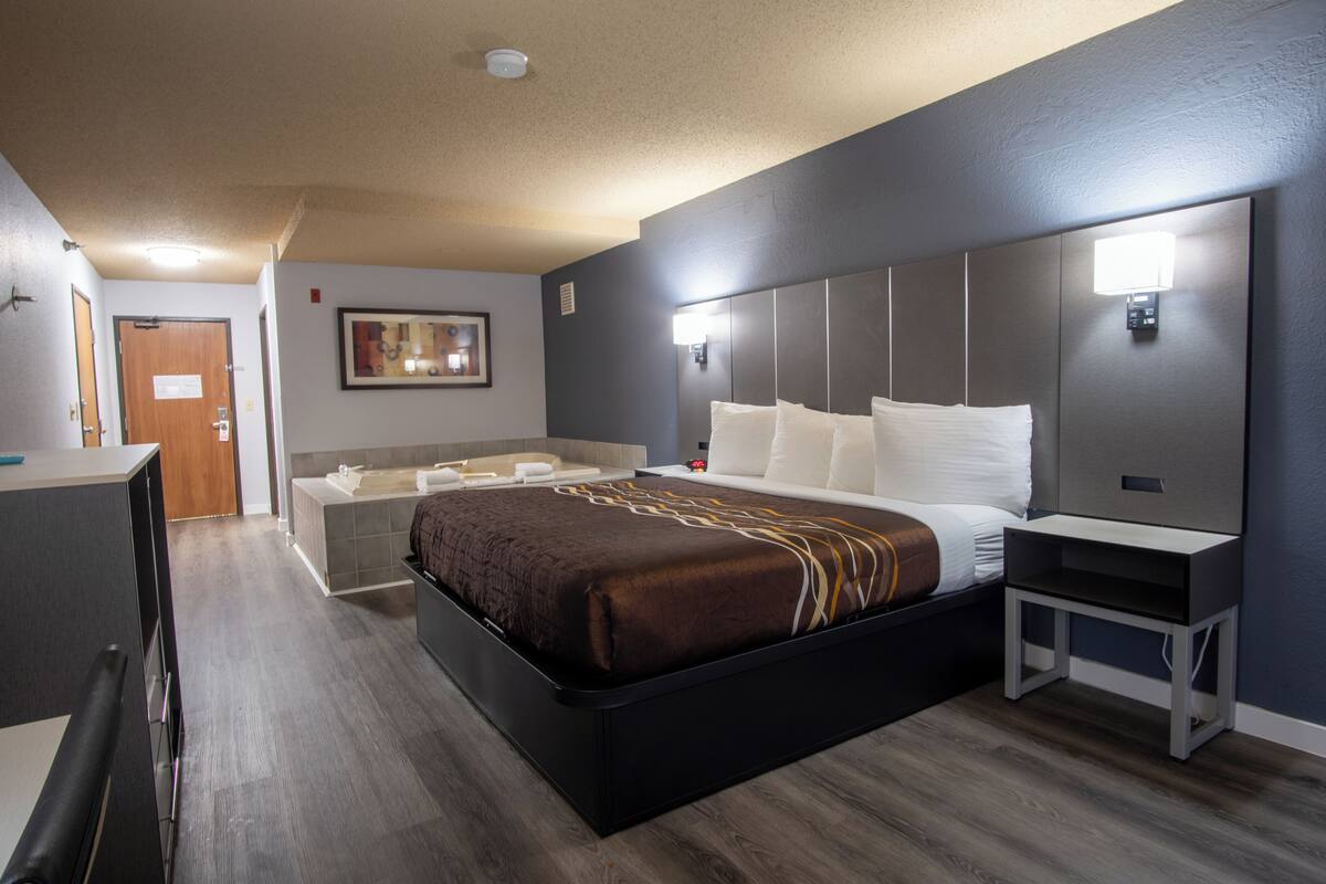 Quarto de hotel moderno com uma cama grande, mesa de cabeceira, escrivaninha e banheiro com banheira.