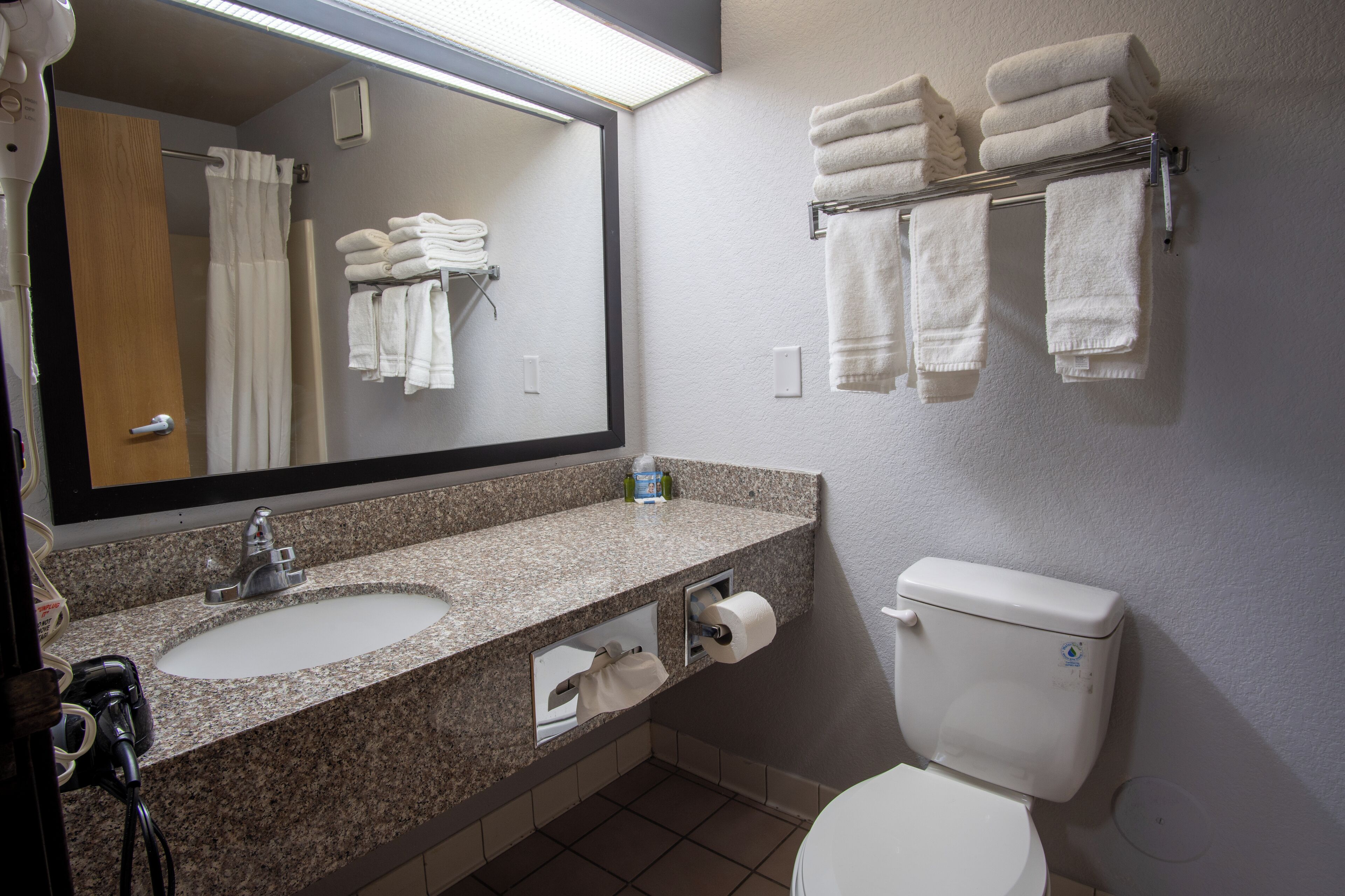 A bathroom with a granite countertop sink, a mirror, a toilet, and a towel rack with folded towels.