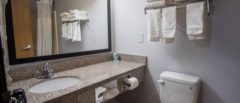 A bathroom with a granite countertop sink, a mirror, a toilet, and a towel rack with folded towels.