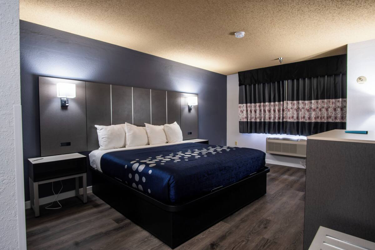 A modern hotel room with a large bed, bedside tables, a desk, and a window with curtains.