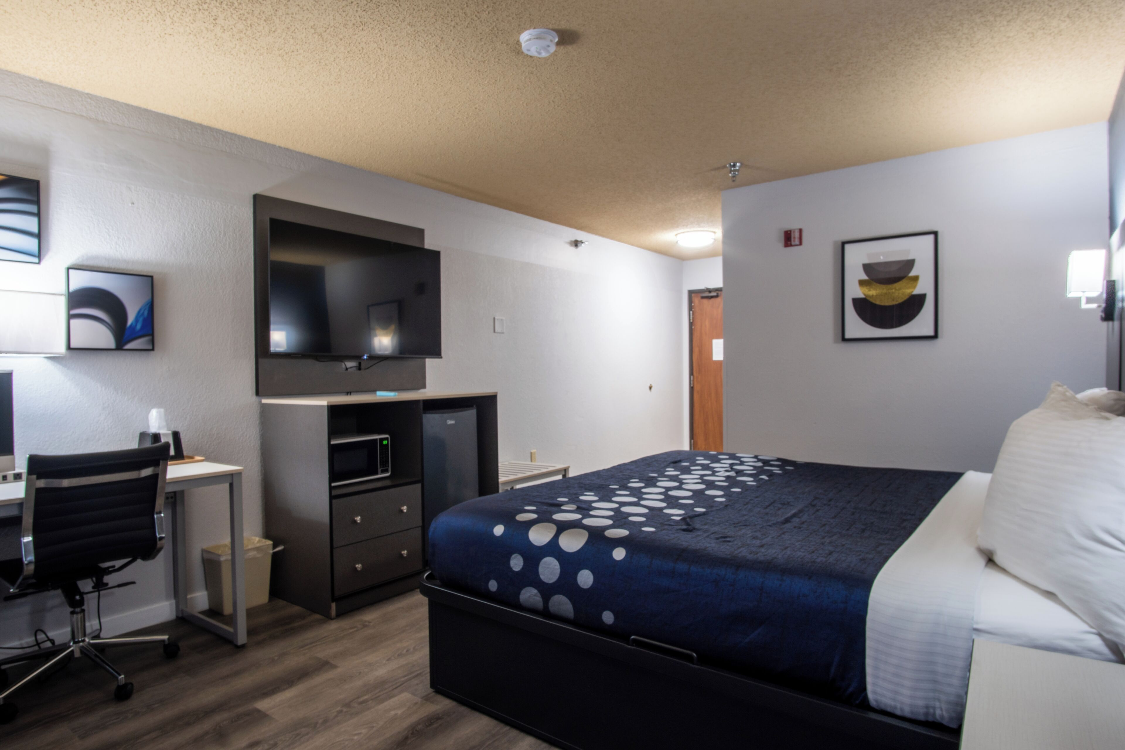 A modern hotel room with a bed, desk, and television.