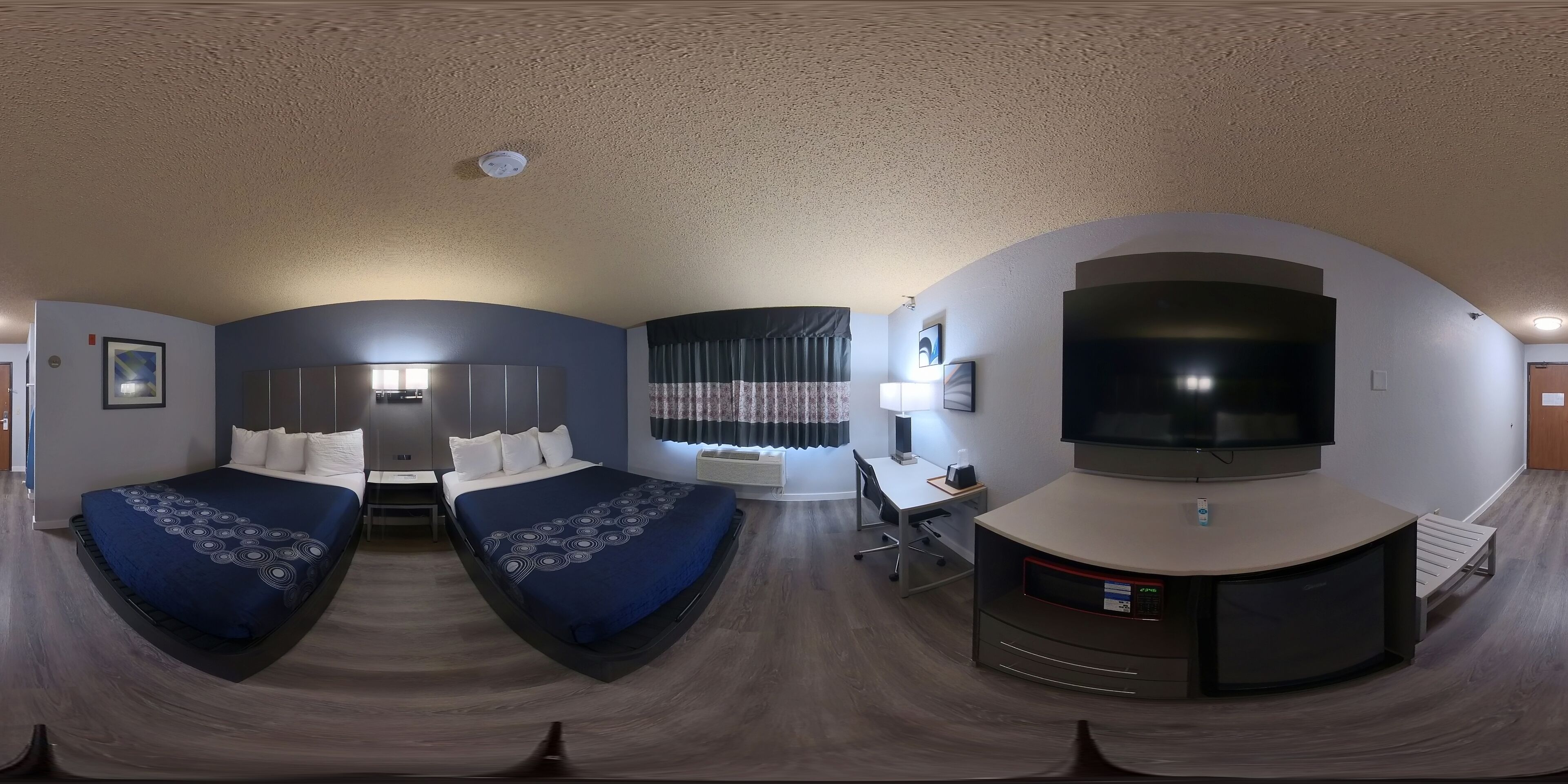 A room with two beds, a desk, a TV, and a curved seating area.