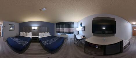 A room with two beds, a desk, a TV, and a curved seating area.