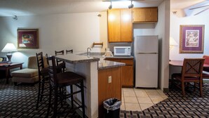 A compact kitchen with wooden cabinets, a microwave, and a refrigerator. There is a small dining area with a table and chairs. - Blue Way Inn & Suites Minneapolis Airport Eagan - Mall of America (Eagan)