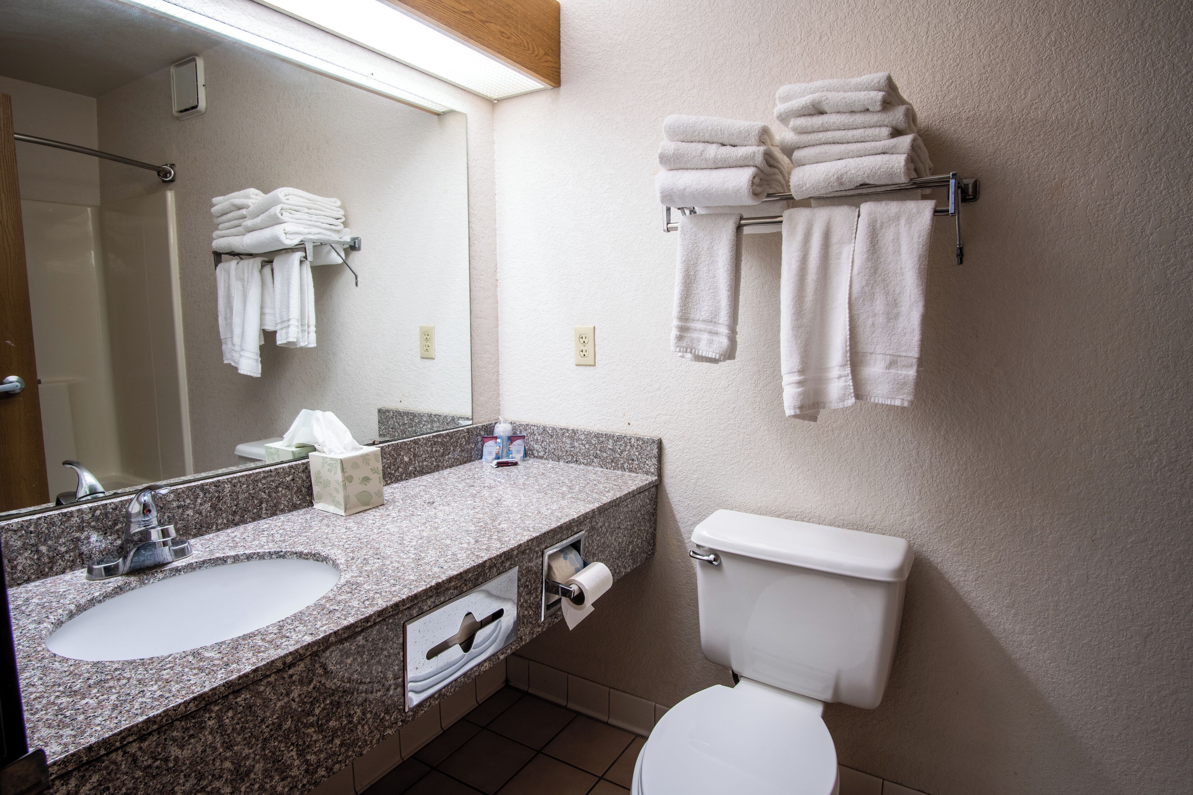 Un baño con lavamanos, espejo, toallero, inodoro y dispensador de toallas.