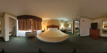 Una habitación de hotel con una cama grande, televisión, escritorio con silla, cómoda y espejo.