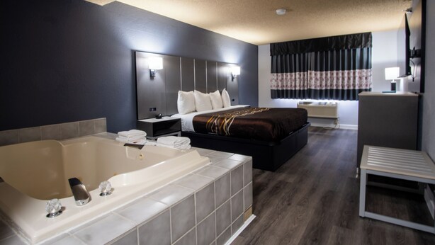 A modern hotel room with a large bathtub, a bed with a dark headboard, a bedside table, and a nightstand. - Blue Way Inn & Suites Minneapolis Airport Eagan - Mall of America (Eagan)