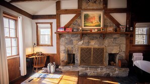 Una sala de estar acogedora con chimenea de piedra, vigas de madera, un sofá cómodo y una estantería.