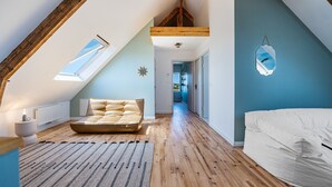 Une chambre confortable située sous les toits, avec un plafond en pente, un grand lit, une lucarne et une vue sur la pièce adjacente.