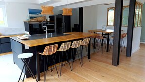 Une cuisine moderne avec un îlot central en bois, des tabourets de bar noirs et des luminaires suspendus.