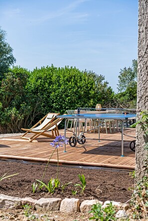 A deck with a table and chairs, surrounded by greenery and a tree.