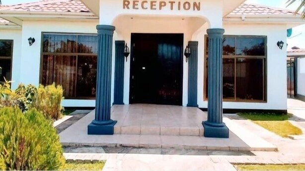 A building with a reception area, featuring a tiled roof, large windows, and blue columns. - Marbella lodge  (Bagamoyo)