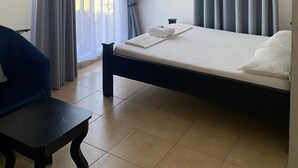 A hotel room with a bed, a desk, a ceiling fan, and curtains. - Marbella lodge  (Bagamoyo)