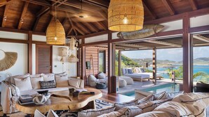 Amplia sala de estar con piscina, techo de madera y grandes ventanales con vistas al mar.