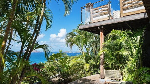 Area esterna tropicale con un solarium in legno, mobili in vimini e vegetazione lussureggiante.
