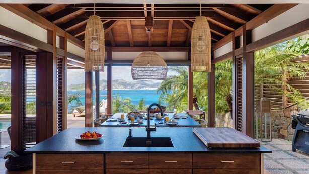 Cocina con vistas al océano, que cuenta con una isla grande, lámparas colgantes de mimbre y una pared de piedra.