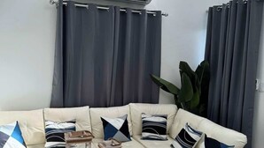 Ein modernes Wohnzimmer mit einer Eckcouch, einem Glastisch und einer großen Klimaanlage über den Vorhängen.