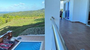 Ein Balkon mit Pool, Blick auf grüne Hügel und klarem Himmel.