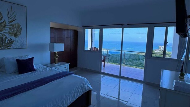 Ein Schlafzimmer mit Bett, Nachttisch, Fernseher und Meerblick.