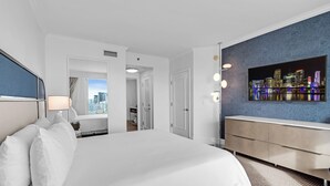 Ett hotellrum med en stor säng, en tv som är monterad på väggen, utsikt över staden och ett modernt badrum.