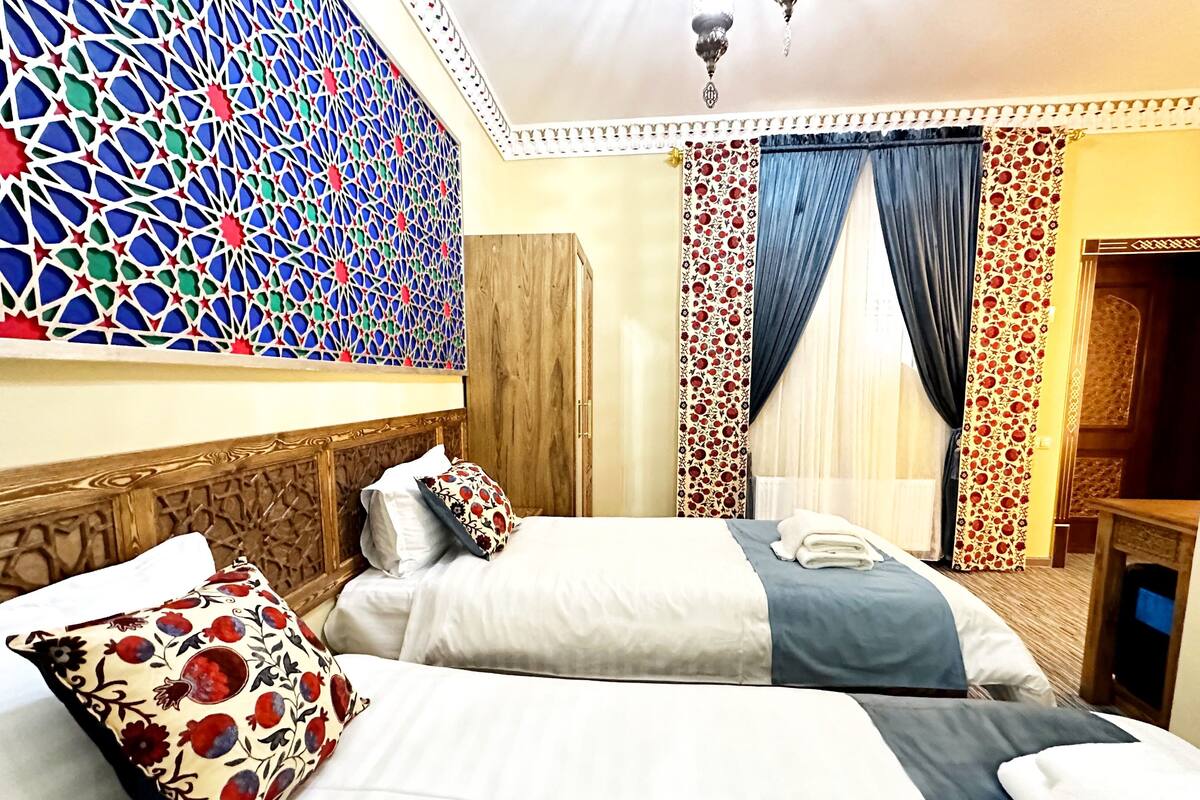 Quarto de hotel com duas camas, um painel decorativo, um guarda-roupa e vista para o exterior através de cortinas.