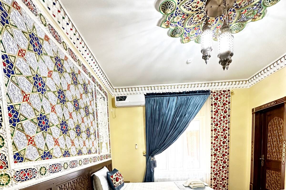 Quarto de hotel com duas camas, teto decorativo e uma janela grande com cortinas.