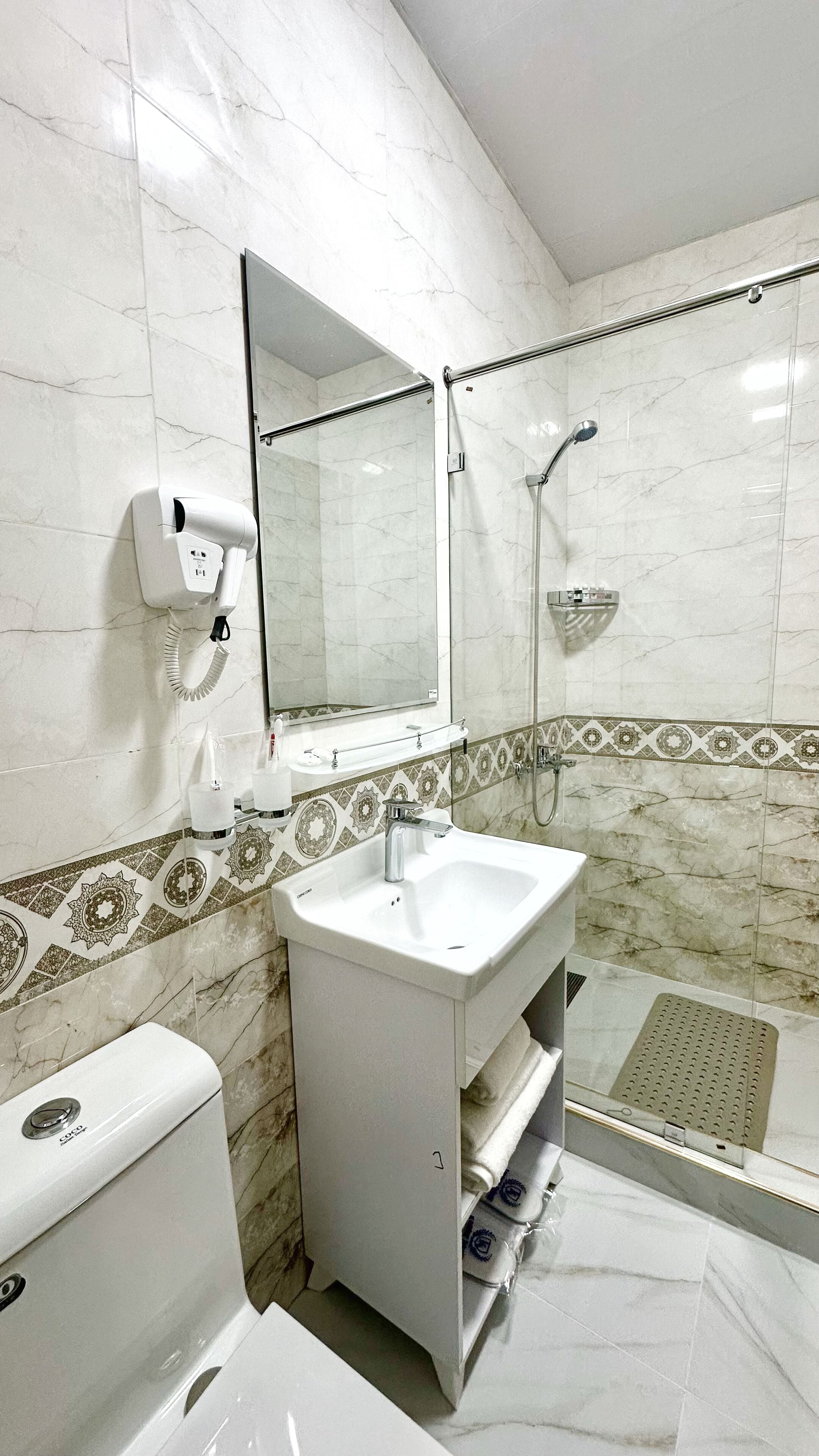 A bathroom with a white sink, a mirror, a handheld showerhead, and a toilet.