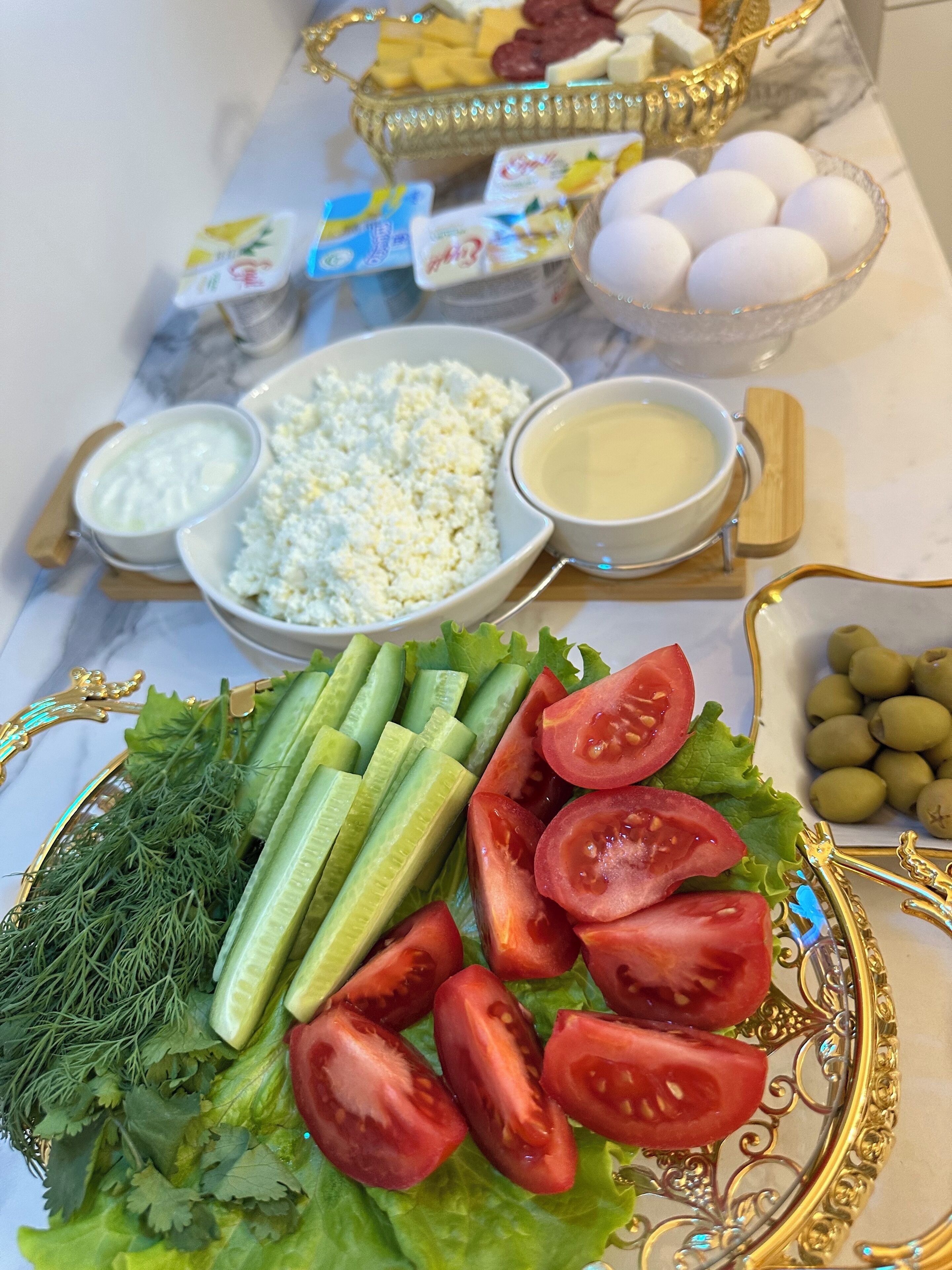 Una mesa con diversos alimentos, como pepinos, tomates, lechuga y aceitunas.