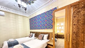 A hotel room with two beds, a decorative ceiling, a patterned wall, and a wooden wardrobe. - Daro Hotel (Bukhara)