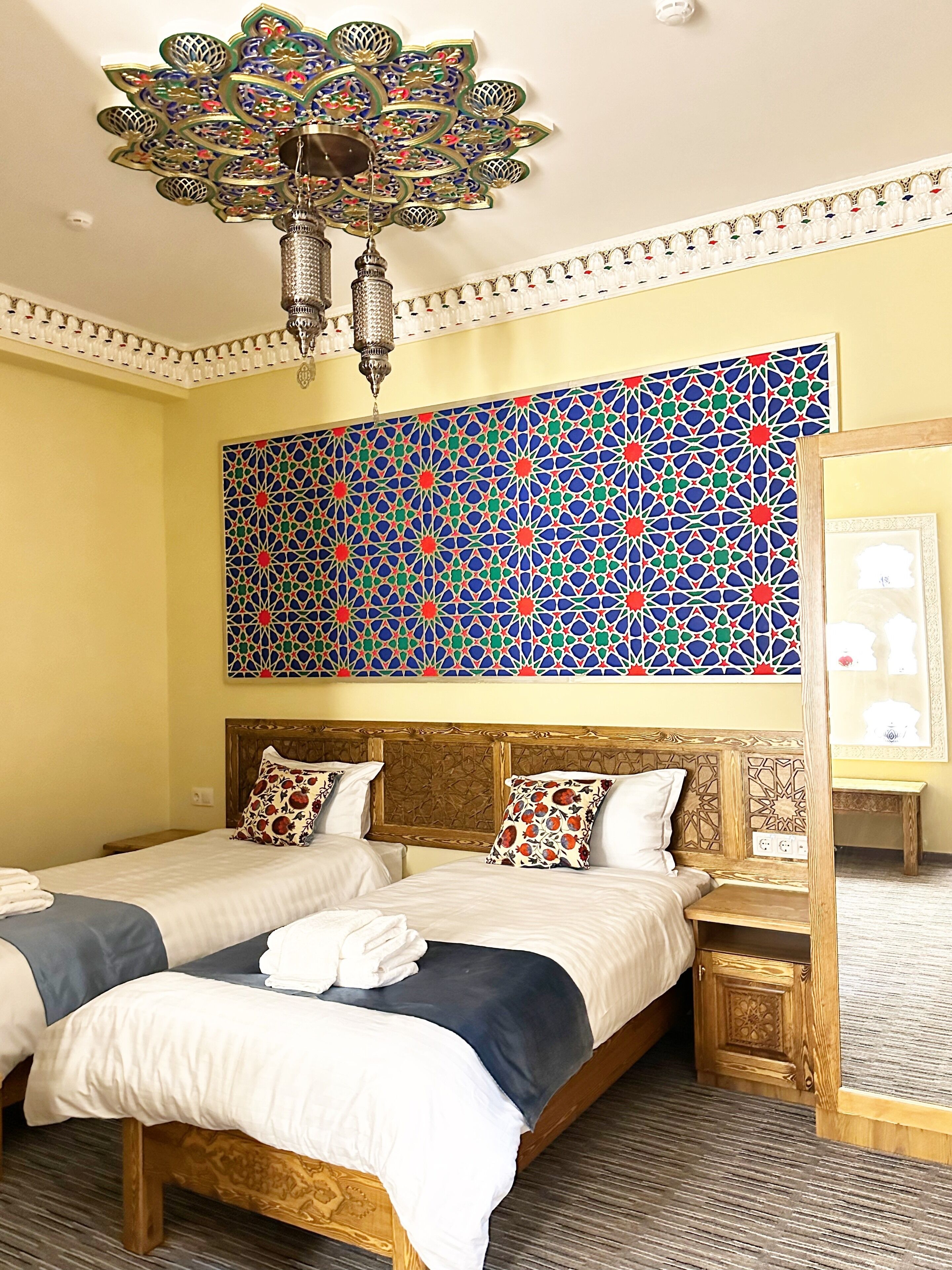 A hotel room with two beds, a decorative chandelier, and a large geometric-patterned wall.