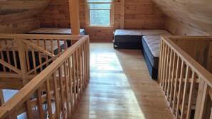 A wooden cabin with a loft bedroom, a window, and a wooden railing. -  3-bedroom Log Cabin with AC, WiFi ,Southwest Harbor
That Rents SAT-SAT ONLY (Southwest Harbor)