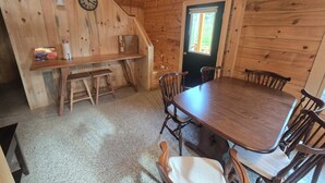 A wooden cabin interior with a dining table, chairs, a bench, a clock, and a door leading outside. -  3-bedroom Log Cabin with AC, WiFi ,Southwest Harbor
That Rents SAT-SAT ONLY (Southwest Harbor)