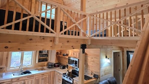A wooden cabin interior with a kitchen area, a dining table, and a loft space. -  3-bedroom Log Cabin with AC, WiFi ,Southwest Harbor
That Rents SAT-SAT ONLY (Southwest Harbor)
