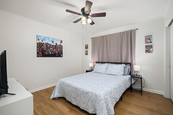Un dormitorio con cama, ventilador de techo, obras de arte y televisor.