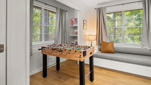 Una habitación con mesa de futbolín, un sofá y una ventana con persianas.