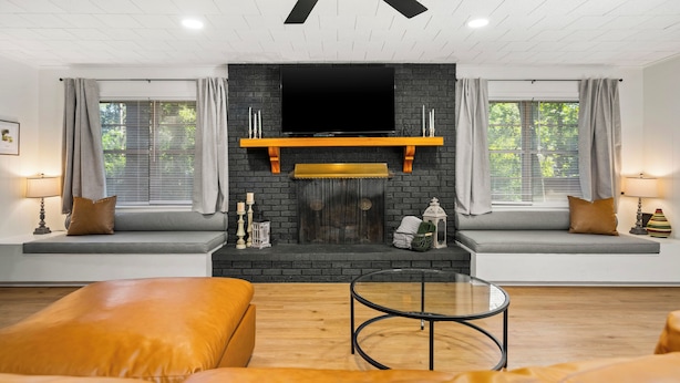 Una sala de estar moderna con chimenea, ventilador de techo y una televisión grande montada encima.
