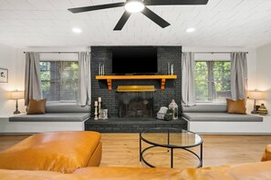 Una sala de estar moderna con chimenea, ventilador de techo y una televisión grande montada encima.