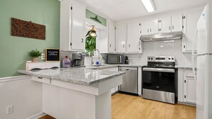 Cocina moderna con armarios blancos, encimera de granito, electrodomésticos de acero inoxidable y una pared de acento verde.