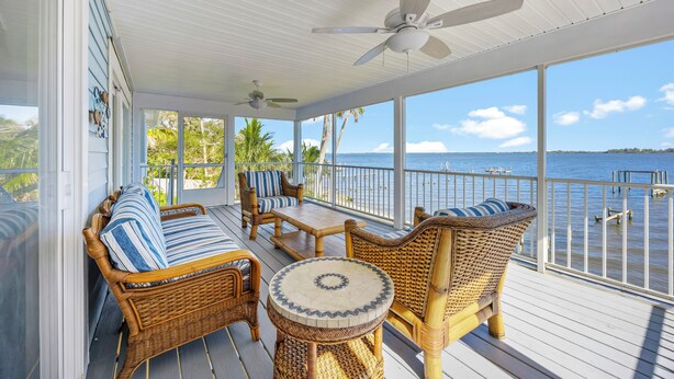 A covered outdoor deck with wicker furniture, a ceiling fan, and a view of the ocean. - Beautiful Direct Riverfront Paradise Home (Micco)