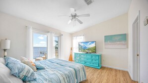 A bedroom with a bed, a TV, a ceiling fan, a window with curtains, and a painting on the wall. - Beautiful Direct Riverfront Paradise Home (Micco)